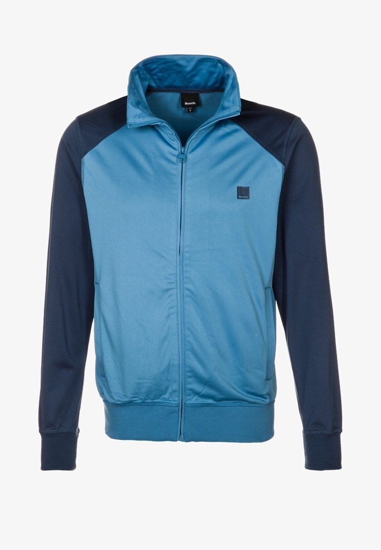 Träningsjacka i blått och marinblått. Har dragkedja framtill, hög krage, ribbade ärmslut och logotyp på vänster bröst. Mjuk textur.