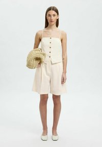 Lystfarvet to-delt outfit bestående af en ærmeløs skjorte med knapper og løse shorts. Tilbehør inkluderer en vævet taske. Glat tekstur.
