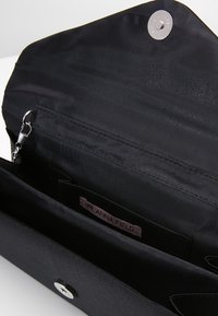 Czarna torebka kopertówka z zapięciem na zatrzask, wyposażona w jedną główną przegrodę, małą kieszonkę na zamek oraz metkę z logo w środku. Gładka struktura.