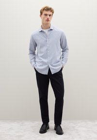 Camicia a quadretti azzurri e bianchi, abbinata a pantaloni scuri e scarpe nere. Vestibilità casual, con maniche lunghe e colletto classico.