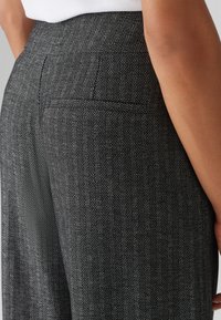 Grijze broek in houndstooth-patroon met een aansluitende taille, platte voorkant en subtiele achterzakdetails. Gemaakt van een gestructureerde, geweven stof.