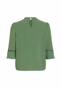 Blouse verte avec manches cloche 3/4, finition décorative près des poignets et petite fermeture boutonnée en forme de goutte dans le dos au niveau de l'encolure.