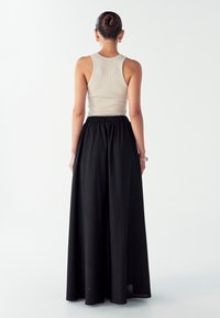 Črna maksi krila z elastiko v pasu, v kombinaciji z ribanim bež topom. Gladek tekstil, preprost dizajn in brez vidnih vzorcev.