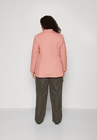 Blazer in light pink fabric with a notch collar, paired with loose-fitting olive green cargo trousers featuring side pockets.