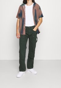 Košile s krátkým rukávem s přechodem barev v hnědé a zelené, doplněná o zelené cargo kalhoty a bílé tenisky. Jednoduchý, ležérní outfit.