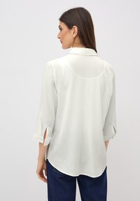Lichtgrijze blouse van structuurstof met een kraag, driekwart mouwen en aan de zijkanten splitten bij de manchetten.
