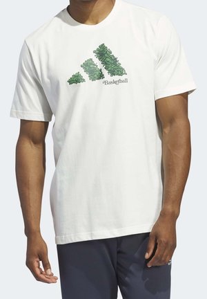 Mężczyzna w białej koszulce z zielonymi liśćmi tworzącymi logo adidas oraz napisem "Basketball", w ciemnych sportowych szortach.