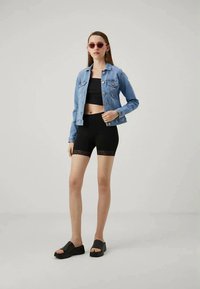 Denim jacket, black crop top, and black lace-trim shorts. Model wears pink sunglasses and black platform slides. Simple, modern styling.