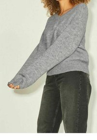 Hellgrauer, lockerer Strickpullover mit langen Ärmeln und geripptem Saum, kombiniert mit dunklen Jeans. Sichtbare Struktur und weiches Material.