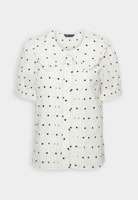 Vit blus med svarta prickar, med en stor rund krage, korta ärmar och ett strukturerat, skrynkligt tyg. Knappstängning fram.