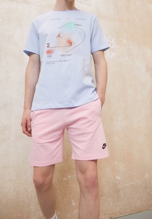 Light blue cotton t-shirt featuring graphic print, round neckline, and short sleeves. Paired with pink shorts and black Nike logo.