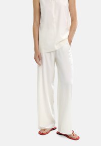 Białe, zwiewne, szerokie spodnie połączone z bezrękawną, lekką koszulą, do tego czerwone klapki na pasek palców. Gładka faktura.