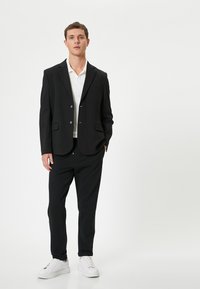 Blazer nero con due bottoni frontali, rever a punta e tasche laterali, abbinato a pantaloni neri abbinati e sneakers bianche.