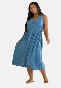 Denim A-line mekko vaaleansinisessä, jossa on V-pääntie, etupainikkeet ja kerätty vyötärö. Sujuva tekstuuri ja hulmuava hame.