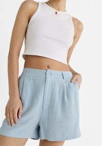 Top cropped bianco abbinato a pantaloni corti plissettati blu chiaro con chiusura a bottone, texture liscia e vestibilità comoda.