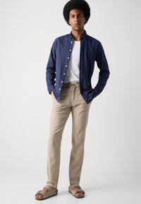 Button-up navy shirt over a white t-shirt, beige drawstring pants, and brown sandals. Features a relaxed fit and soft textures.