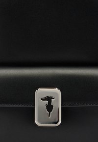 Černá kožená taška s hladkým povrchem. Obsahuje obdélníkovou stříbrnou sponu s vyřezávaným designem, který zvyšuje celkovou estetiku.