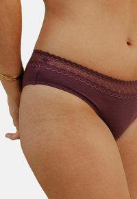 String en coton bordeaux avec une taille en dentelle texturée arborant un bord festonné. Le tissu est lisse avec des coutures minimales.