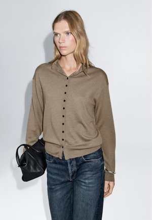 Brown knit sweater with a button-up front, long sleeves, and a soft texture. Paired with dark blue denim jeans and a black handbag.