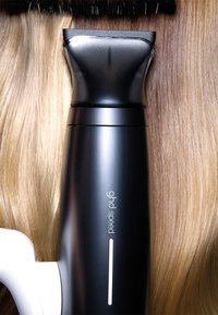 Lisseur à cheveux ghd noir et blanc sur des mèches de cheveux blonds lisses et brillants.