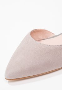 Chaussure plate en daim gris clair avec bout pointu et doublure intérieure beige douce sur fond blanc.