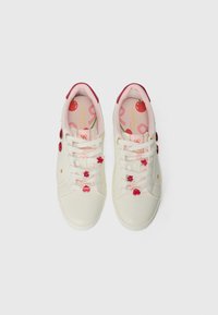 Valkoiset sneakersit, joissa on vaaleanpunaisia yksityiskohtia, koristeelliset sydämen ja kukkien yksityiskohdat nauhoissa, kultaiset yksityiskohdat ja kuvioitu vaaleanpunainen sisäpohja.