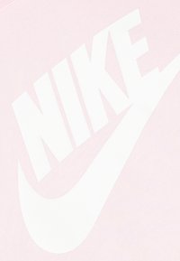 Jasnoróżowa koszulka Nike z dużym białym logo i znakiem Swoosh. Miękka w dotyku z gładkim wykończeniem, z naciskiem na wyraźne elementy brandingowe.