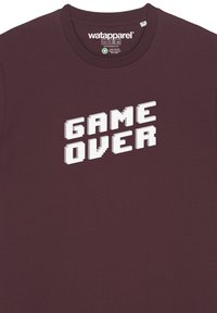 Bordeauxrotes Baumwoll-T-Shirt mit kurzen Ärmeln, das den Text "GAME OVER" in großen, pixeligen weißen Buchstaben zeigt.