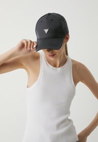 Granatowa czapka baseballowa z materiału, z srebrnym trójkątnym logo z przodu, posiadająca zakrzywiony daszek i tonowe detale przeszycia.