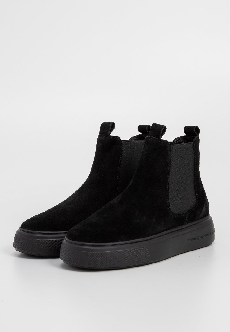 Stivali Chelsea in suede nero con pannelli laterali elasticizzati, linguette e una suola in gomma nera texturizzata. Finitura liscia con un design minimalista.