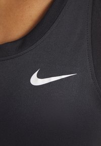 Gros plan sur un tissu de sport noir Nike avec un logo blanc Nike swoosh près de l'encolure sur le haut de la poitrine d'une personne.