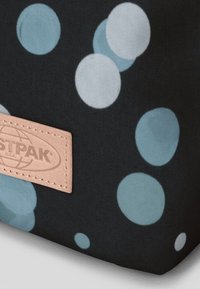 Svart tygpåse med ljusblåa prickar, med en beige läderetikett som har ett präglat logotyp. Slät struktur med rundad form.