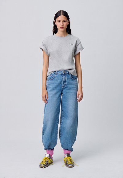 T-shirt grigia a maniche corte con risvolti, jeans blu larghi, calze rosa e sneaker grigie con lacci gialli. Design semplice e vestibilità comoda.