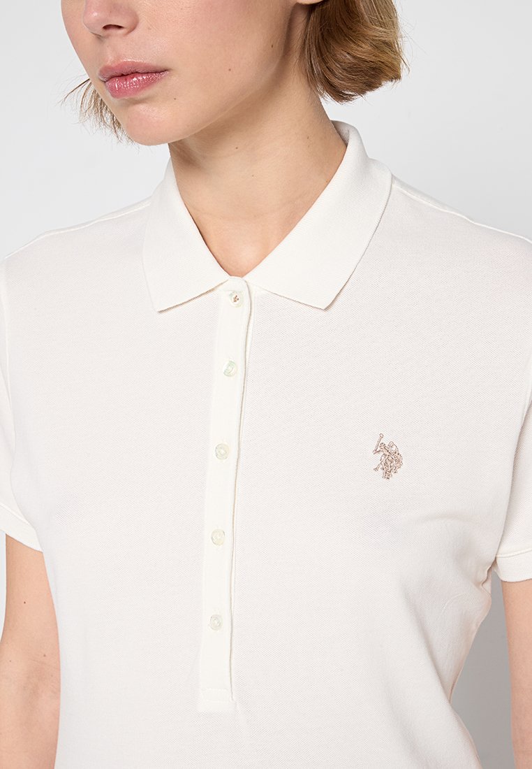 Polo shirt color crema realizzato in tessuto testurizzato con colletto classico, dotato di una patta con cinque bottoni e di un piccolo logo ricamato sul petto.