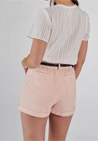 Weißes Kurzarm-gestreiftes Oberteil mit Spitzenbesatz, kombiniert mit rosa, hochgekrempelten Denim-Shorts mit Gesäßtaschen und besticktem Detail.
