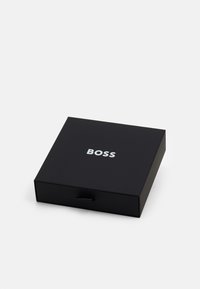Cutie neagră cu un finisaj mat, având un logo argintiu "BOSS" pe partea superioară. Cutia are un tab pentru deschidere.