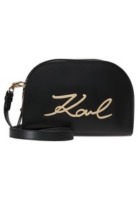 Czarna skórzana torebka o zaokrąglonym kształcie, z charakterystycznym złotym napisem "Karl" na froncie, smukłym, regulowanym paskiem oraz gładką fakturą.