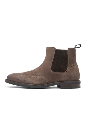 Stivaletto Chelsea in camoscio marrone con dettagli brogue, pannello laterale elastico, linguetta al tallone e tacco basso impilato su suola nera.