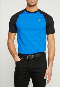 T-shirt bleu à manches courtes avec des manches raglan noires, en coton, présentant un petit logo sur la poitrine et un col rond.