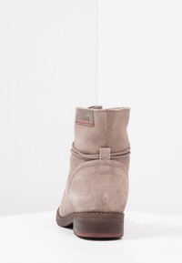 Light gray suede ankle boot with a rounded toe, low stacked heel, and decorative tie detail on the side. Features a brown sole.