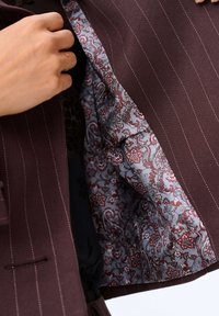 Burgundowy żakiet o prążkowanej powierzchni; widoczne wzorzyste szare i czerwone wnętrze w paisley. Posiada klapę wyciętą i zapięcie na jeden guzik.