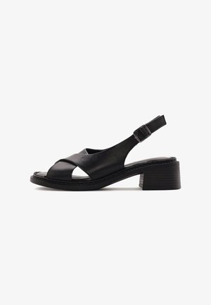 Sandale slingback en cuir noir avec un bout ouvert, un design à lanières croisées et un petit talon carré. La semelle présente des rainures subtiles.