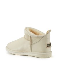 Botas de tobillo color crema hechas de cuero con un suave forro de piel, suela plana y una etiqueta de marca en la parte trasera. Textura suave, diseño minimalista.