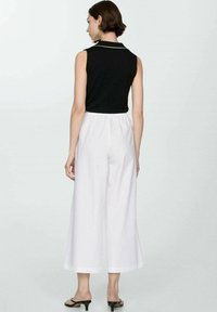 Crna majica bez rukava s bijelim ovratnikom, uparena s labavim bijelim culottes hlačama. Outfit ima opušteni kroj i glatku tkaninu. Crne sandale upotpunjuju izgled.