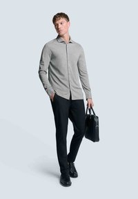 Graues langärmliges Hemd mit Knöpfen, schwarze Hose und schwarze Ledertasche; glatte Textur, taillierte Passform, kontrastierende Knöpfe und Kragenakzente.