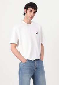 Hvid bomulds T-shirt med rund halsudskæring og korte ærmer, der har et lille logo-patch i rød, hvid og blå på venstre bryst.