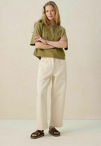 T-shirt cropped vert olive, coupe décontractée. Pantalons larges crème avec poches arrière. Sandales foncées avec brides tissées, semelle plate.
