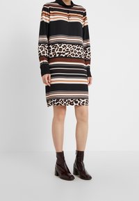 Black dress with horizontal stripes in brown, beige, and cream, featuring a leopard-patterned band at the hem. Long sleeves and collar detail.