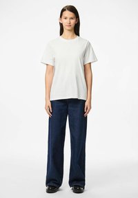 Valkoinen puuvillainen t-paita lyhyillä hihoilla, yhdistettynä löysästi istuviin tummiin farkkuihin, joissa on suora leikkaus ja minimaalinen yksityiskohtaisuus.