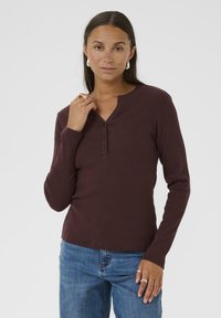 Burgundowa longsleeve koszulka henley z okrągłym dekoltem, trzema guzikami oraz prążkowaną teksturą, w połączeniu z niebieskimi dżinsami.